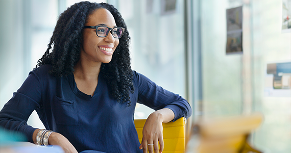 A newly hired young woman sits in an office and smiles at an offscreen HR Manager explaining her new benefits