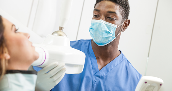 Un higienista dental ajusta la posición de la máquina de rayos X para capturar mejor una radiografía de los dientes de un paciente