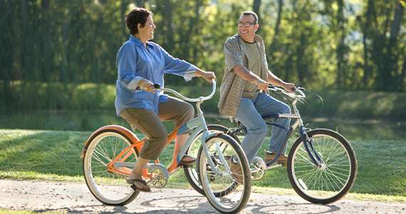 A middle-aged couple chat while they ride their bikes leisurely along a path on a sunny day 