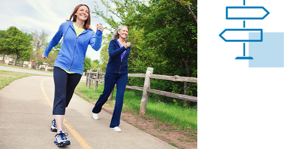 Two middle-aged women are smiling as they power walk down a paved path outside; next to them is a line art signpost